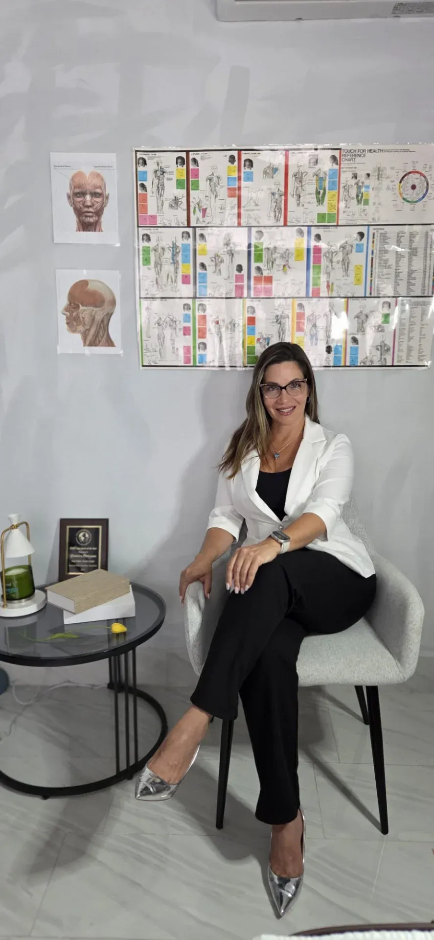 Yahaira Rodríguez sentada en su consulta, frente a la tabla de referencia de Touch for Health